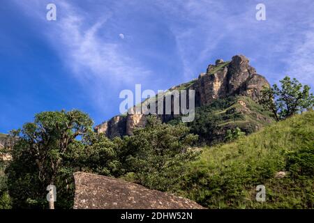 Mountain jutting on rocky hill against blue skies and greenery in Drakensburg, South Africa Stock Photo