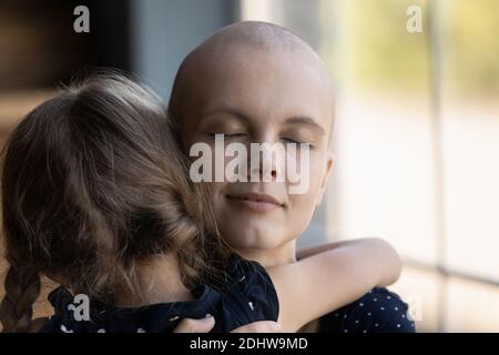 Close up loving sick hairless mother hugging little daughter Stock Photo