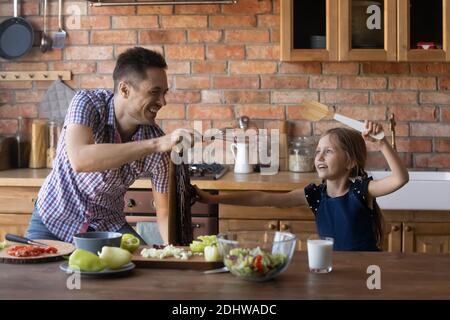 Happy father and little daughter playing with utensils in kitchen Stock Photo