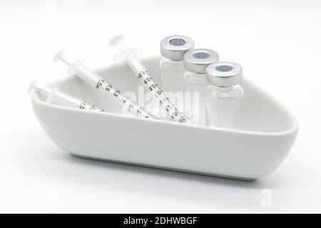 Three Medical vaccine syringes and Three medical ampules in a medical ceramic dish on a white background. Stock Photo