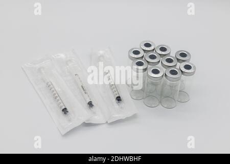 Ten medical vaccine ampules and Three syringes in their plastic packets on a white background The syringes are sealed and unopened as are the ampules. Stock Photo