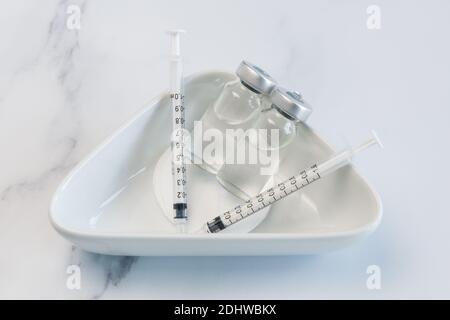Two PartsVaccine Ampules and Two Syringes lying loosely in a Medical ceramic container. Stock Photo
