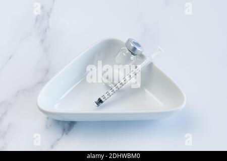 One Vaccine Ampule and One Syringe lying loosely in a Medical ceramic container. Stock Photo
