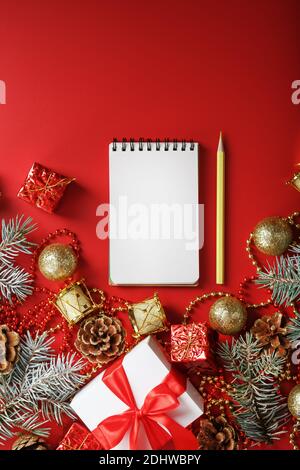 Christmas composition with notepad and a pencil for writing wishes with Christmas tree decorations on a red background. Christmas mood and plans for t Stock Photo