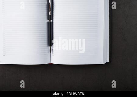 Black Notepad with a black pen on a black background. Top view, minimalistic concept. Free space. Stock Photo