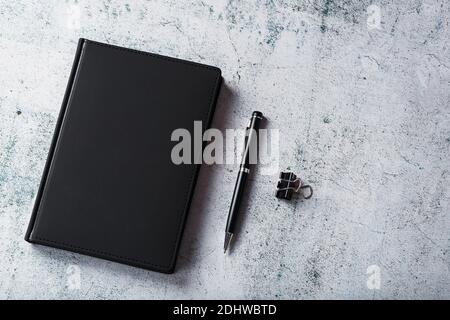 Office desk with black notepad and pen on gray background. Top view with copy space. Business goals and objectives concept Stock Photo