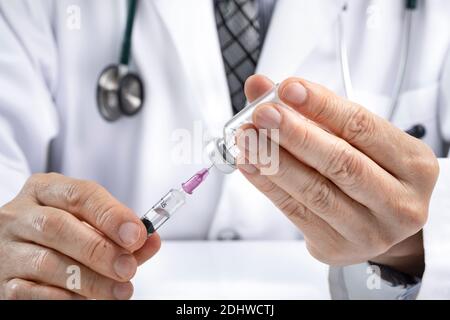 A male doctor using a syringe to draw fluid or vaccine from a vial. Medication or vaccination administration concept. Covid vaccine concept. Asian eth Stock Photo