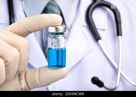 A doctor in white coat holding a medicine vial containing blue liquid.  Vaccine, vaccination concept fighting against virus covid-19. Stock Photo