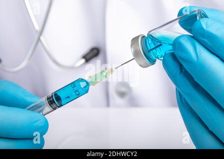 A doctor in white coat drawing clear light blue liquid from a vial into a syringe. Medication or vaccine adminstration, covid-19 prevention concept. Stock Photo