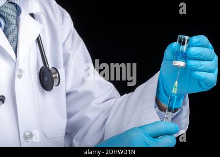 A doctor in white coat drawing clear light blue liquid from a vial into a syringe. Medication or vaccine adminstration, covid-19 prevention concept. D Stock Photo