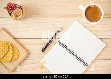 A blank notebook and a cup of coffee in white ceramic cup. Wooden background. Stock Photo