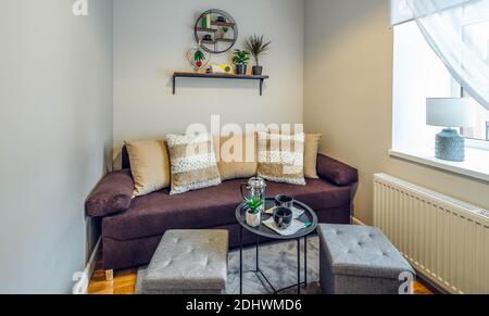 Contemporary interior of small living room in new flat. Cozy couch. Black coffee table. Flowers on wall shelf. Stock Photo