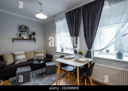 Modern interior of small studio apartment. Laid table on two persons. Cozy couch with cushions. Home decor. Stock Photo