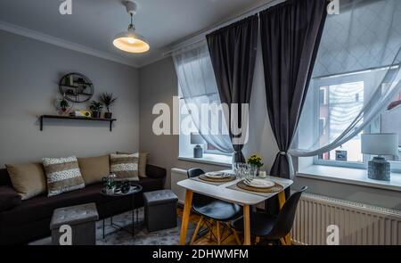 Modern interior of small studio apartment. Laid table on two persons. Cozy couch with cushions. Home decor. Stock Photo