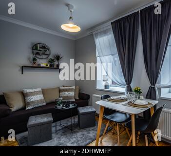 Modern interior of small studio apartment. Laid table on two persons. Cozy couch with cushions. Home decor. Stock Photo