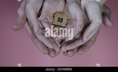 The hands of the mother and father with the child hold the figure in the form of a house on a pink background. Stock Photo