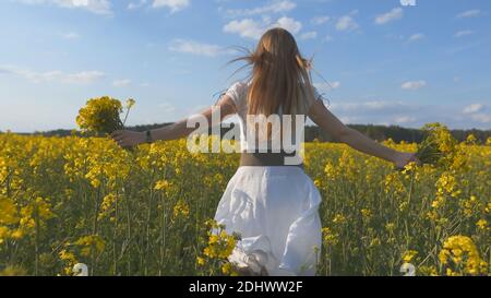 A girl in a white dress runs among a rapeseed field. Stock Photo