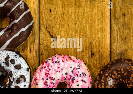 Colorful donuts on wooden table. Sweet icing sugar food with glazed sprinkles, doughnut with chocolate frosting. Top view with copy space Stock Photo