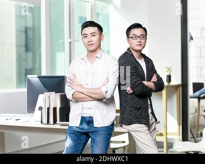 two young asian entrepreneurs standing in office looking at camera with arms crossed Stock Photo