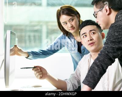 team of young asian people discussing business in office using desktop computer Stock Photo