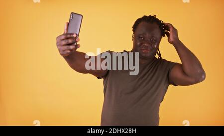 Man taking selfie. African american black model using smartphone to take picture of him self against yellow background. High quality photo Stock Photo