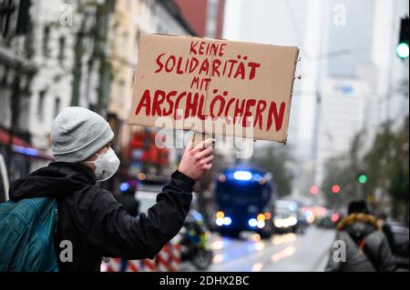 12 December 2020, Hessen, Frankfurt/Main: A counter-demonstrator holds up a cardboard sign saying 'No solidarity with assholes'. Despite a ban on the 'lateral thinkers' demonstration, numerous people have gathered in the city centre. 'Lateral thinkers' and 'antifascists' are separated by a massive police presence. Photo: Andreas Arnold/dpa Stock Photo