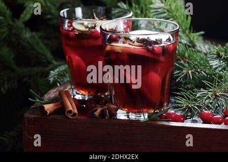 Mulled red wine with cranberry, apple and spices: anise, cinnamon, rosemary and cloves on dark moody black background and fir branches, winter christm Stock Photo