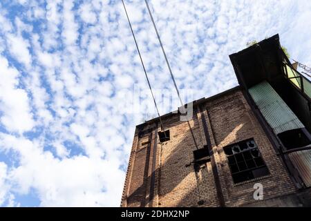 Abandoned industrial building, dirty brick exterior, broken out windows, green corrugated fiberglass against blue sky and clouds copy space, horizonta Stock Photo