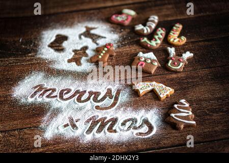 Gingerbread cookies and Merry Christmas greetings text in icing sugar on wood table background Stock Photo