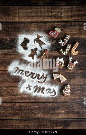 Gingerbread men cookies and 'Merry Christmas' greetings text in icing sugar on wood table background from above Stock Photo
