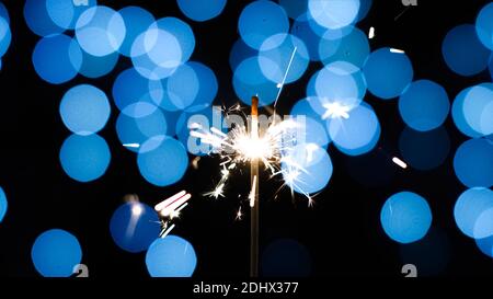 Holiday sparkler against blue lights background. Festive decoration for christmas new year. Stock Photo