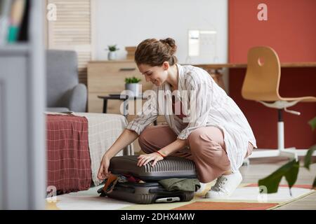 Young woman packing her clothes and closing her suitcase in the room she preparing for business trip Stock Photo