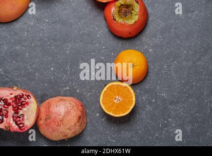 Top view of orange, with grapefruit, pomegranate, passion fruit and kaki on dark grey stone background arranged in circle. Healthy and fresh fruits Stock Photo