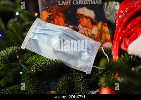 Viersen, Germany - December 9. 2020: Close up of surgical face protection mask in christmas fir tree with blurred Wham last christmas song vinyl recor Stock Photo