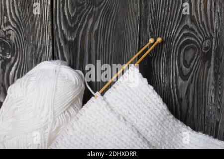 Knitting with needles. Wooden knitting needles and white threads. On black pine boards. Stock Photo