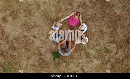 Friendly family waving hands while sitting on the grass with a dog. View from the drone. Stock Photo
