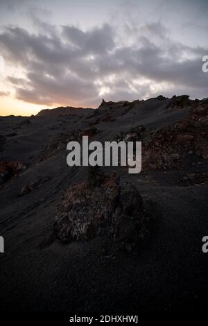 volcanic land with molten lava rocks on a sunset with clouds and a person's footsteps going up the hill Stock Photo