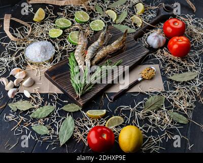 Fresh shrimps on kitchen table board with ingredients. Raw prawns, tomatoes, salt, limes and garlic Stock Photo