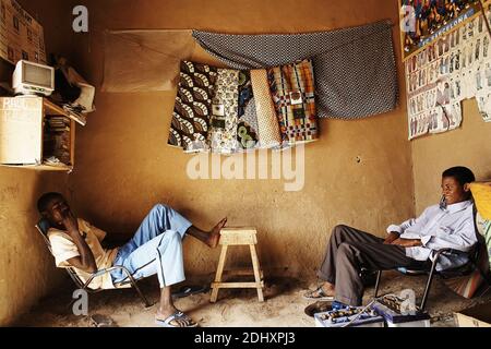 Two tailors sit and rest in their workshop in Mali, West Africa, taking a break from their detailed and skillful work with fabrics and garments. Stock Photo