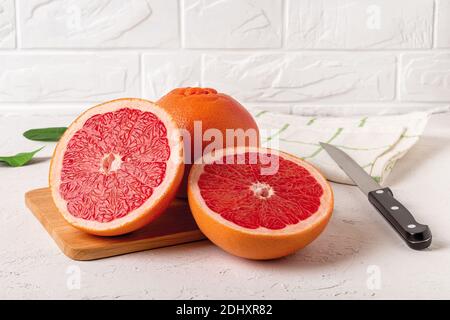 Whole ripe grapefruit and two juicy halves on a cutting board and knife. Ingredient for fruit desserts. Tasty vegetarian food and slimming diet. Stock Photo