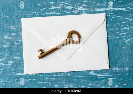 Brown metal shabby vintage key on a white envelope over a turquoise scratched paint surface. Send or receive key in an envelope. Copy space. Top view. Stock Photo