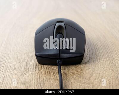 Close-up of black wired optical mouse over brown desk. Work or study at the computer at home or in the office. Front view. Stock Photo