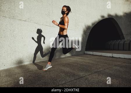 Female athlete on morning running workout. Woman in fitness wear wearing face mask running outdoors. Stock Photo
