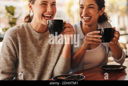 Two friends having coffee together in a coffee shop. Best friends gossing over coffee in a cafe. Stock Photo