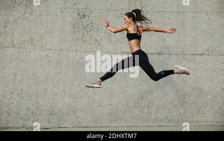 Female athlete running and jumping. Side view of flexible female athlete exercising outdoors. Stock Photo