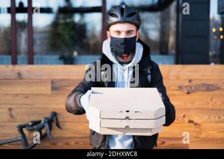 Delivery person holds pizza boxes in a stretched out hand, focus on package. Food delivery, bicycle courier at work, takeaway catering concept Stock Photo