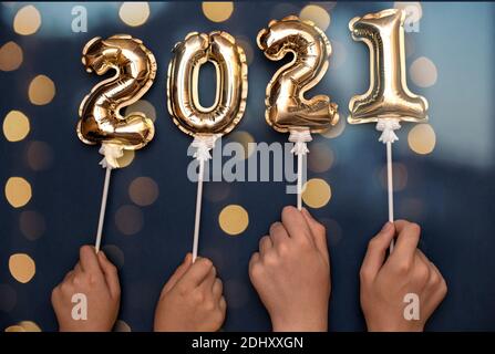 2021 the numbers on the inflated gold balls with bokeh from the lights of the garland hold their hands up.  Stock Photo