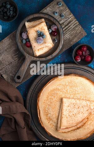 Pancakes with frozen berries on wooden boards on a blue background. Stock Photo