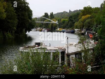 AJAXNETPHOTO. 2019. PORT MARLY, FRANCE. - BRIDGE OVER RIVER SEINE - A NEW PEDESTRIAN AND CYCLIST PASSARELLE BRIDGE CROSSING THE RIVER SEINE AT PORT MARLY TOWERS ABOVE OLD PENICHE HOUSEBOATS MOORED TO THE RIVER BANK. 19TH CENTURY IMPRESSIONIST ARTISTS ALFRED SISLEY, CAMILLE PISSARRO, CLAUDE MONET, AUGUSTE RENOIR, COROT, AS WELL AS FAUVIST EXPRESSIONIST PAINTERS ANDRE DERAIN, MAURICE DE VLAMINCK AND OTHERS MADE STUDIES OF RIVER LIFE NEAR HERE. THE BRIDGE, COMPLETED IN 2016, MEASURES 86M IN LENGTH AND WEIGHS 131 TONNES.PHOTO:JONATHAN EASTLAND/AJAX REF:GX8192609 550 Stock Photo