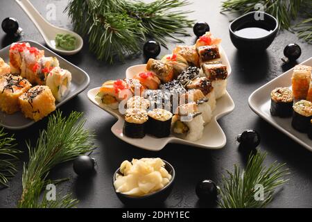 Festive Christmas dinner with sushi set with Xmas decoration on black table. Close up. New Year party. Stock Photo
